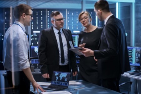 Four business individuals, 3 men and 1 woman, having a discussion in a modern IT office, one man is holding a tablet.